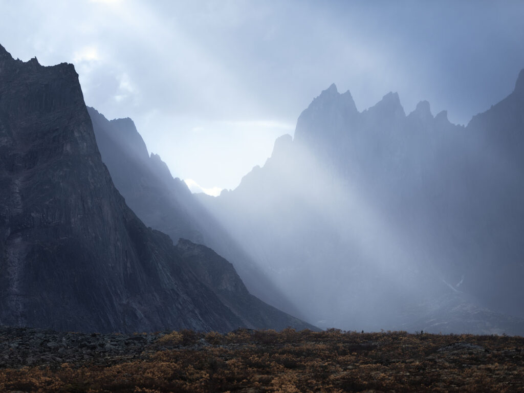 sun shines through storm over jagged mountain peaks