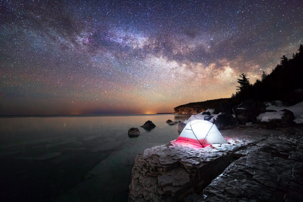 A lit tent under the stars on the shores of lake Huron