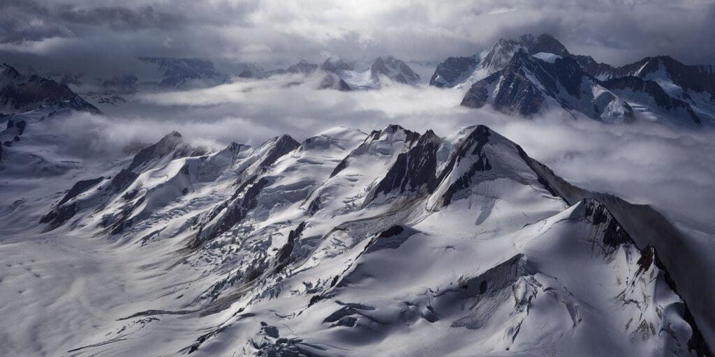 massive mountains and ice fields breaking through low clouds