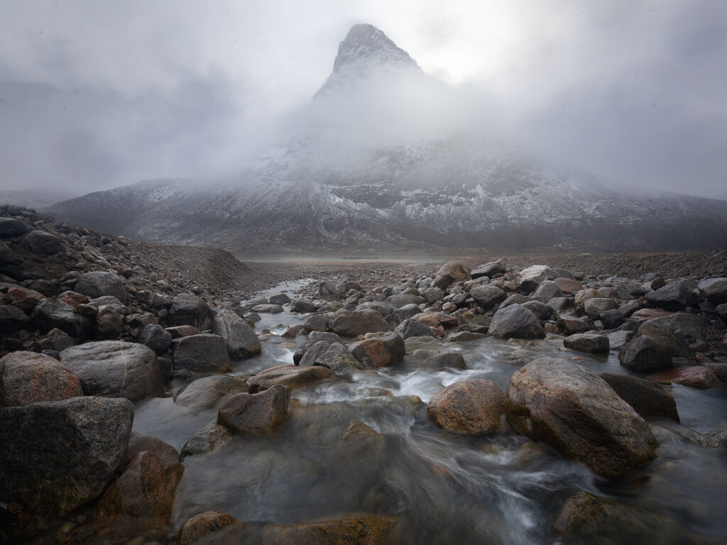 mountain peak pushes through snowy clouds over arctic river